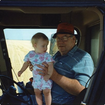 A grandfather holding his baby granddaughter in the cab of a combine harvester